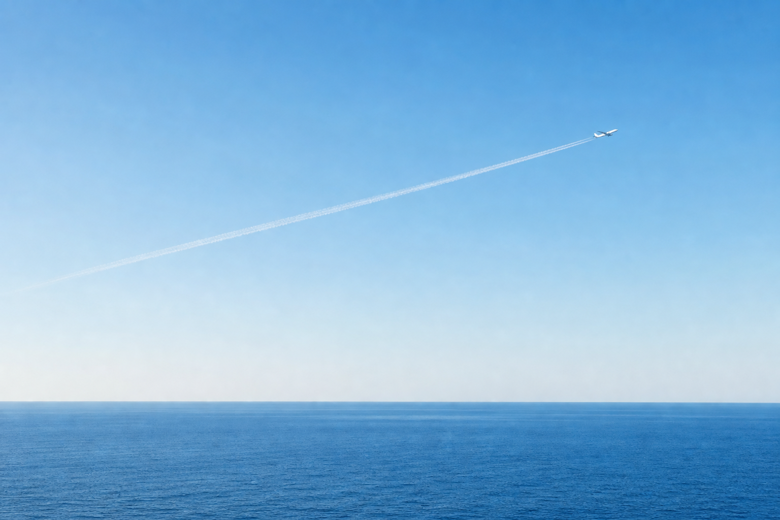 青い空と海の間を、飛行機雲を描きながら飛ぶ飛行機